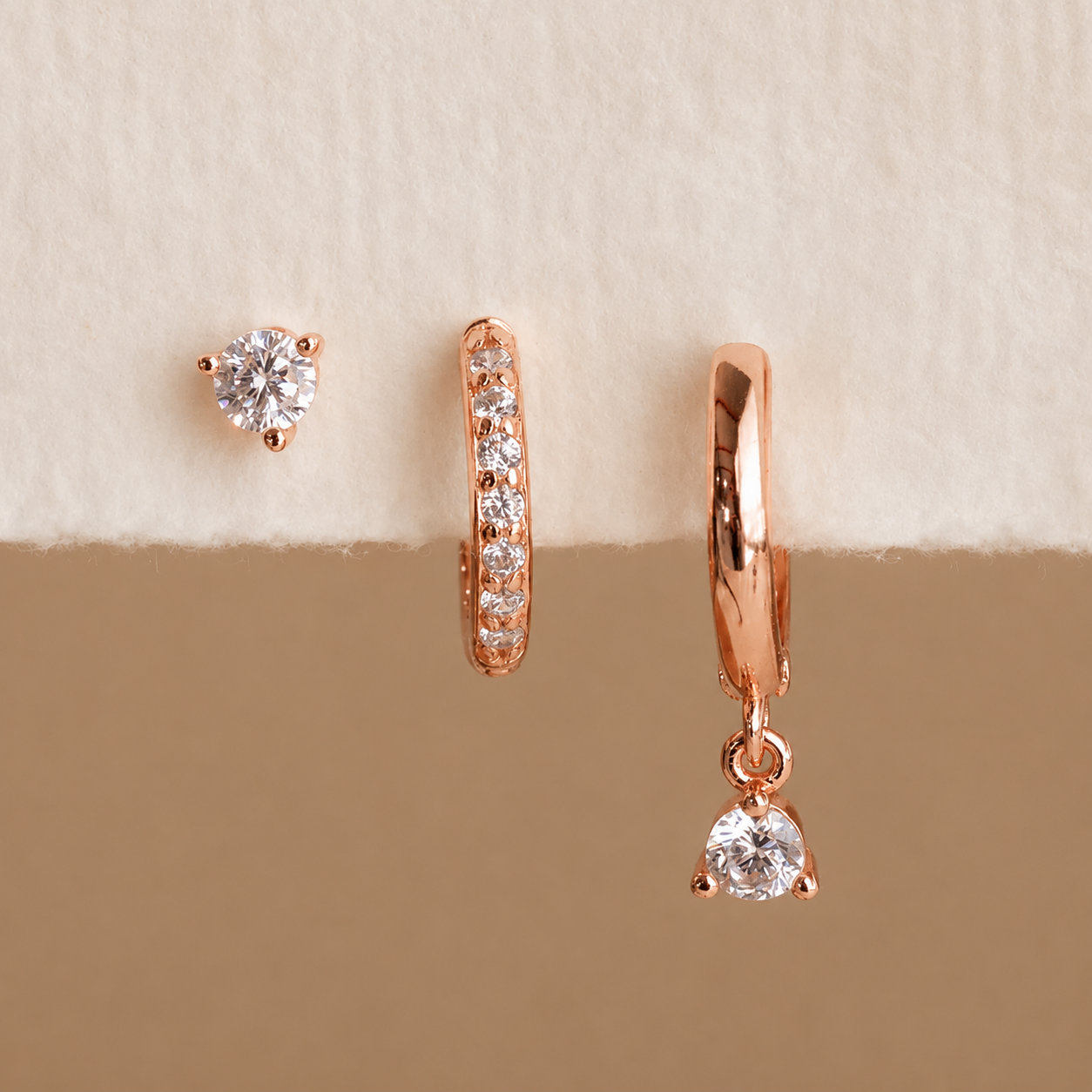 Rose gold diamond earrings on a beige background